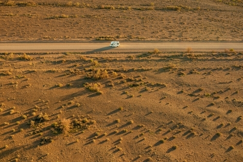 Aerial shot of campervan travelling alone along dirt road in outback