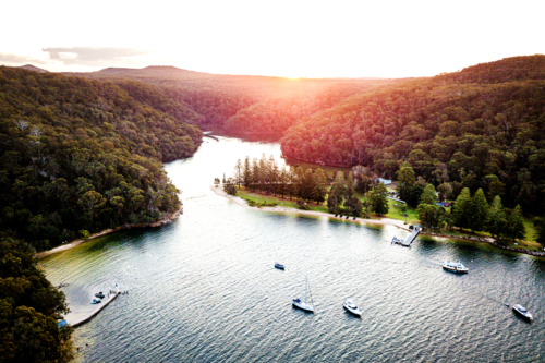 Aerial sunset over sheltered bay with boats and forested shoreline - Australian Stock Image