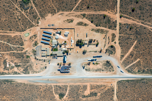 Aerial top-down view of a remote roadhouse with solar panels and trucks by a highway - Australian Stock Image