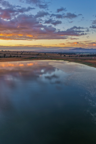 Aerial vertical scene capturing a colourful sunrise over Lake Keepit and the dam wall - Australian Stock Image