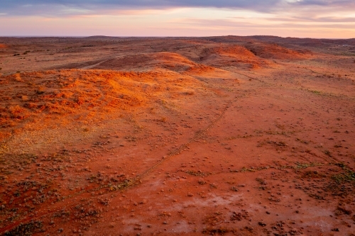 Aerial view a dry orange outback landscape with hills and gullies at sunset