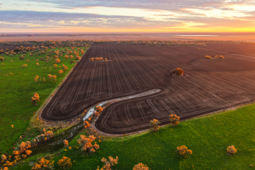 Aerial view capturing warm sunshine over cultivated fields surrounded by lush green countryside - Australian Stock Image