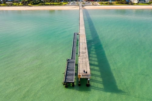 Aerial view looking back along a long narrow jetty towards the beach - Australian Stock Image