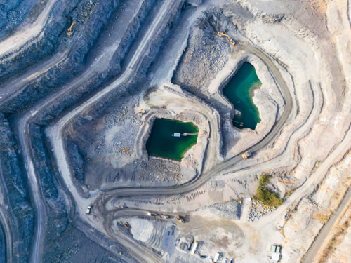Aerial view looking down into a tiered quarry pit with machinery and water ponds - Australian Stock Image