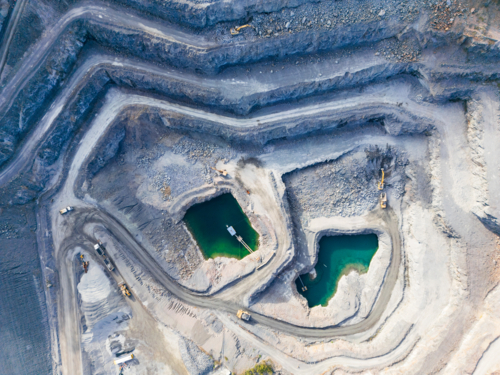 Aerial view looking down into a tiered quarry pit with machinery and water ponds - Australian Stock Image