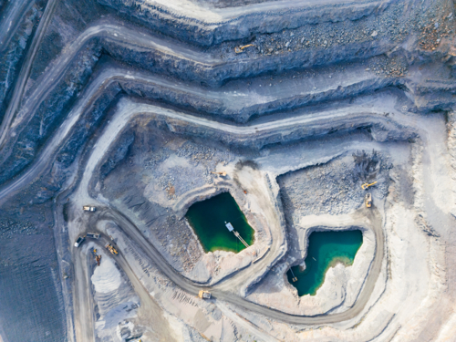 Aerial view looking down into a tiered quarry pit with machinery and water ponds - Australian Stock Image