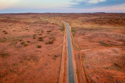 Aerial view of a bitumen road running through and arid outback landscape at twilight - Australian Stock Image