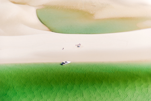 Aerial view of a boat anchored by a remote sandbar with vivid green shallows - Australian Stock Image