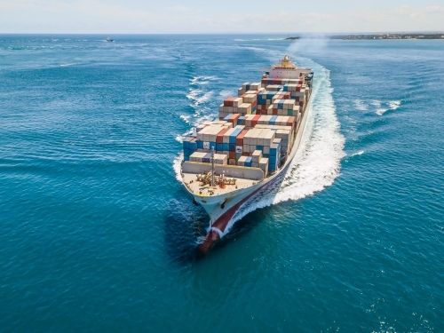 Aerial view of a cargo ship steaming through calm blue water - Australian Stock Image