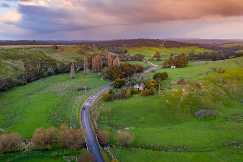 Aerial view of a country road running through green rural countryside under a stormy sky - Australian Stock Image