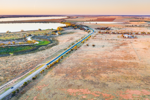 Aerial view of a country road through dry farmland alongside a creek and freshwater lake - Australian Stock Image