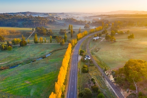 Aerial view of a country road winding through autumn trees at sunrise - Australian Stock Image