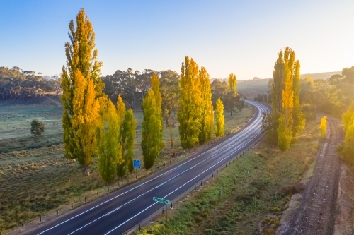 Aerial view of a country road winding through autumn trees - Australian Stock Image