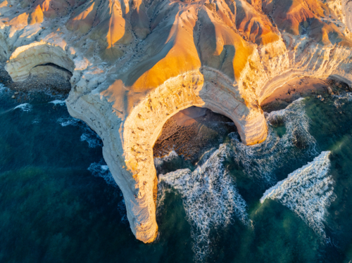 Aerial view of a crescent shaped cove along a rugged eroded coastline on golden evening light - Australian Stock Image