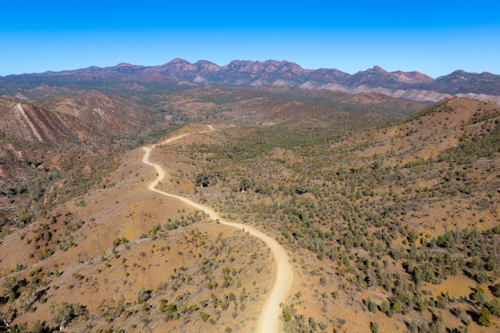 Aerial view of a dirt track curving through an arid valley toward mountains - Australian Stock Image
