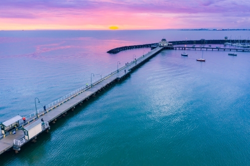 Aerial view of a dramatic purple sunset over a coastal jetty and breakwater