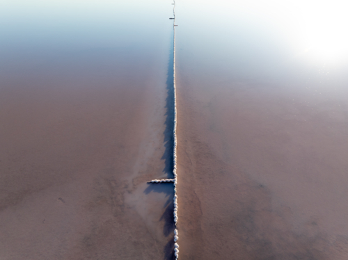 Aerial view of a fence running vertically through a pink salt lake - Australian Stock Image