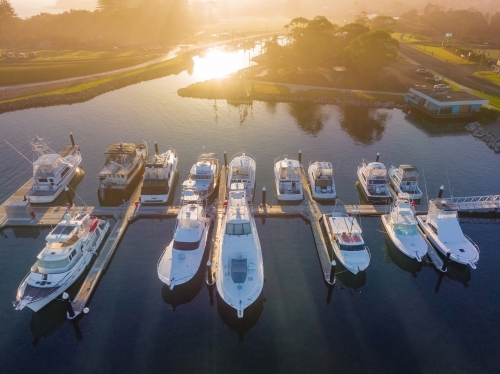 Aerial view of a foggy sunrise over boats moored along jetty in a coastal marina - Australian Stock Image