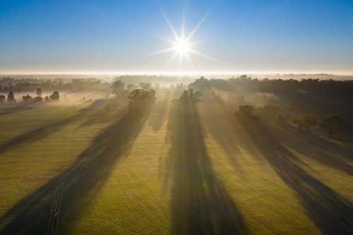 Aerial view of a foggy sunrise with gum trees casting long shadows over farmland at Moama - Australian Stock Image