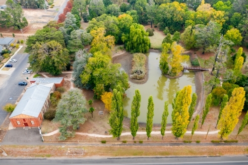 Aerial view of a garden lake surrounded by autumn trees in a country town - Australian Stock Image