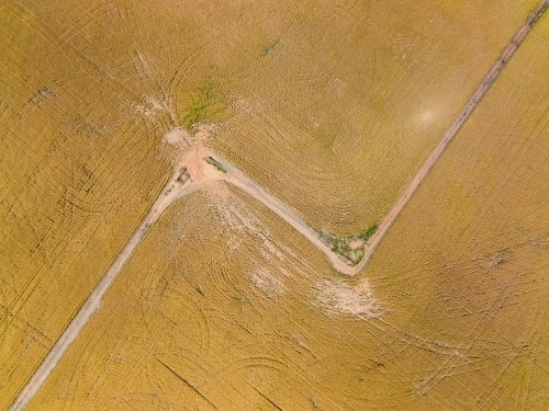 Aerial view of a gateway on the corner of a fence line between two dry paddocks with wheel tracks - Australian Stock Image