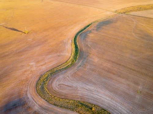 Aerial view of a green creek bed winding through a ploughed paddock at Dimboola in Victoria - Australian Stock Image
