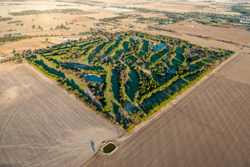 Aerial view of a green golf course surrounded by dry farmland on the edge of a rural town - Australian Stock Image