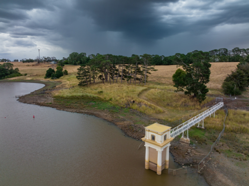 Aerial view of a heavy rain falling over a water tower along the shoreline of a rural reservoir - Australian Stock Image