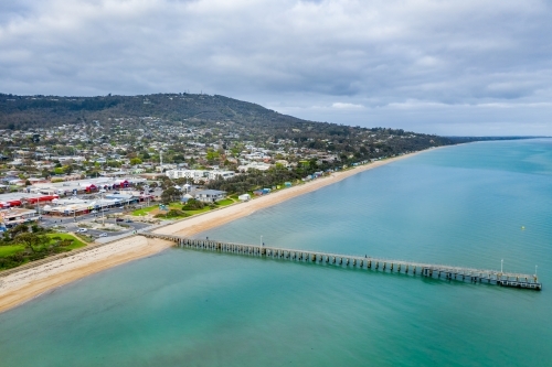 Aerial view of a long narrow jetty out over a calm bay near a coastal town. - Australian Stock Image