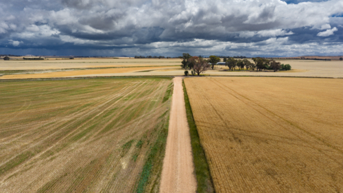 Aerial view of a long straight dirt road through farmland under dark storm clouds - Australian Stock Image