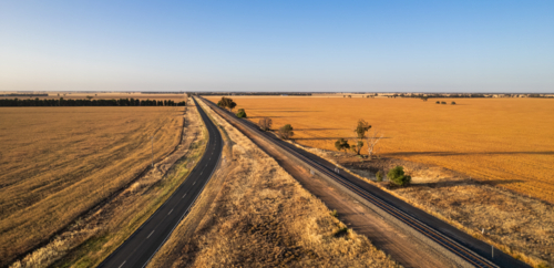 Aerial view of a long, straight road in a vast farmland - Australian Stock Image
