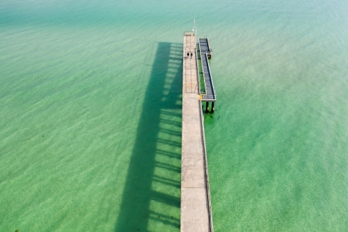 Aerial view of a narrow jetty and its shadow over  calm water - Australian Stock Image