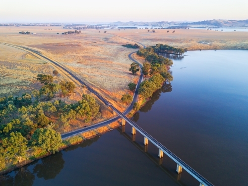 Aerial view of a railway bridge crossing a lake in early morning sunshine - Australian Stock Image