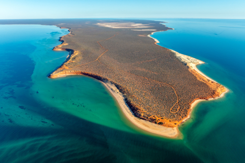 Aerial view of a remote peninsula with red cliffs, turquoise waters and untouched coastline - Australian Stock Image