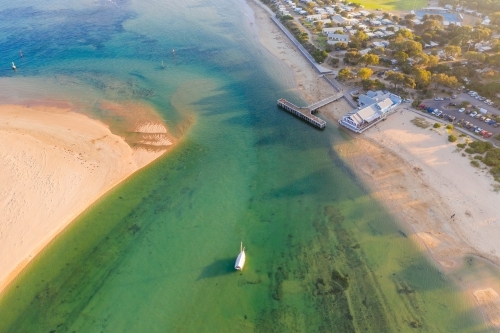 Aerial view of a river flowing through a narrow opening past an jetty and a coastal town - Australian Stock Image