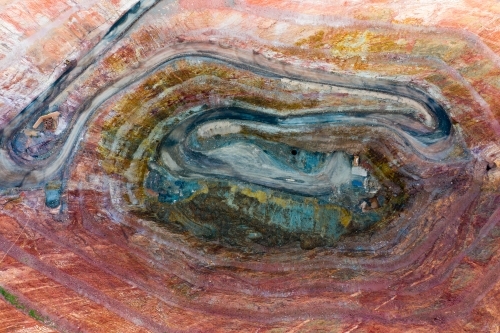 Aerial view of a road winding down into a large open cut mine with various colours of earth
