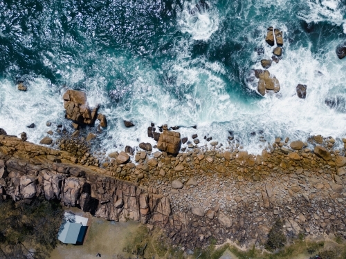 Aerial view of a rocky coastline with a house standing near the cliff - Australian Stock Image