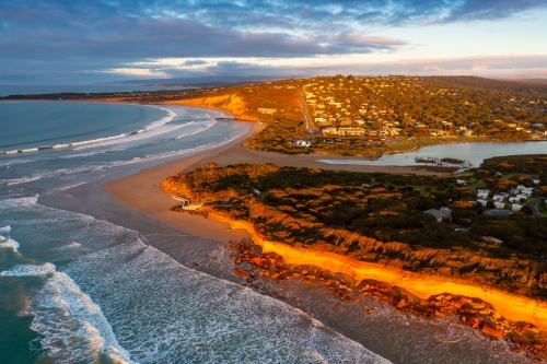 Aerial view of a rugged coastline below a town catching golden dawn side lighting - Australian Stock Image