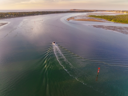 Aerial view of a small boat creating a wake in a wide coastal river - Australian Stock Image