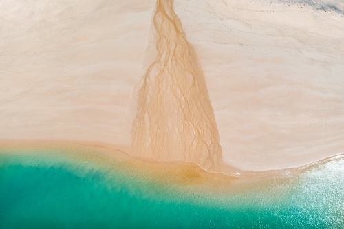 Aerial view of a small creek flowing over a white sandy beach into the sea - Australian Stock Image