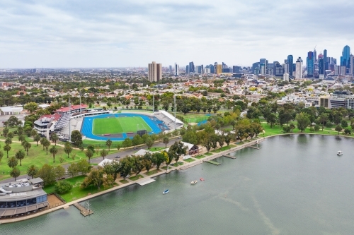 Aerial view of a sporting arena on the shores of a lake in front of a city skyline - Australian Stock Image