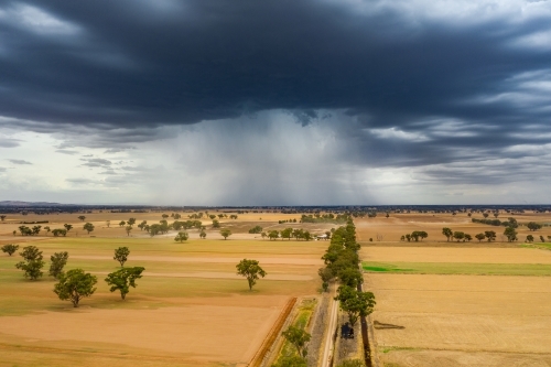Aerial view of a storm cloud dropping rain on dry farmland