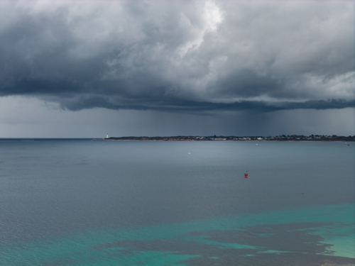 Aerial view of a tiny boat on a calm bay under rain falling from a dark stormy sky - Australian Stock Image