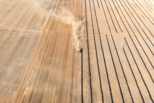 Aerial view of a tractor working through a dry paddock, trailing dust as it creates neat rows across - Australian Stock Image