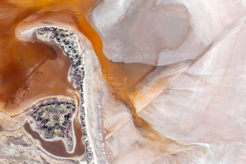 Aerial view of a vivid orange and pink salt lake shoreline with a small vegetated island - Australian Stock Image