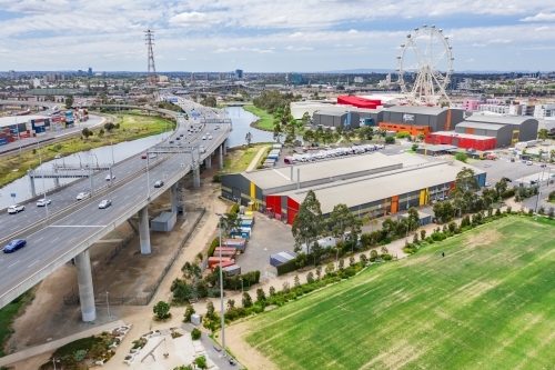 Aerial view of a wide freeway overpass with a sporting field below and ferris wheel in the distance - Australian Stock Image