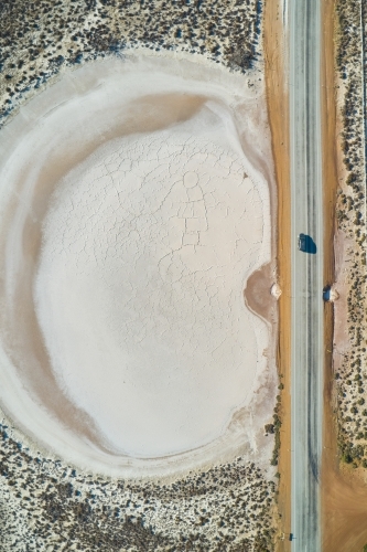 Aerial view of an SUV driving on a bitumen road past a small dry salt lake in rural WA - Australian Stock Image