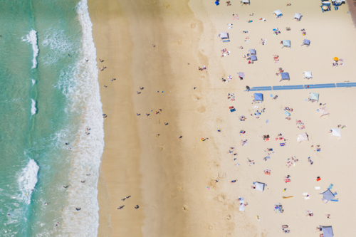 Aerial view of bathers spread over a wide sandy beach above the tide line - Australian Stock Image