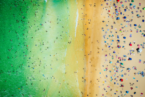 Aerial view of beach with swimmers, umbrellas, and golden sandy shoreline - Australian Stock Image