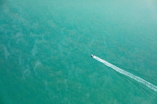aerial view of boat heading out in blue green sea - Australian Stock Image